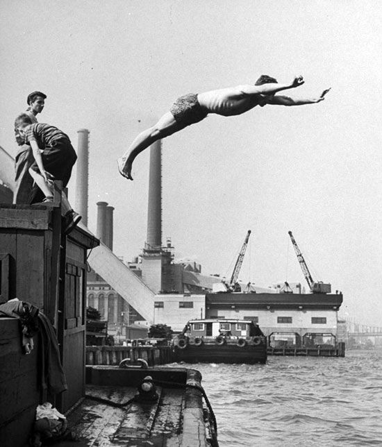 "Boy diving from top of building on wharf, poised in air over river." New York, NY. June 1947